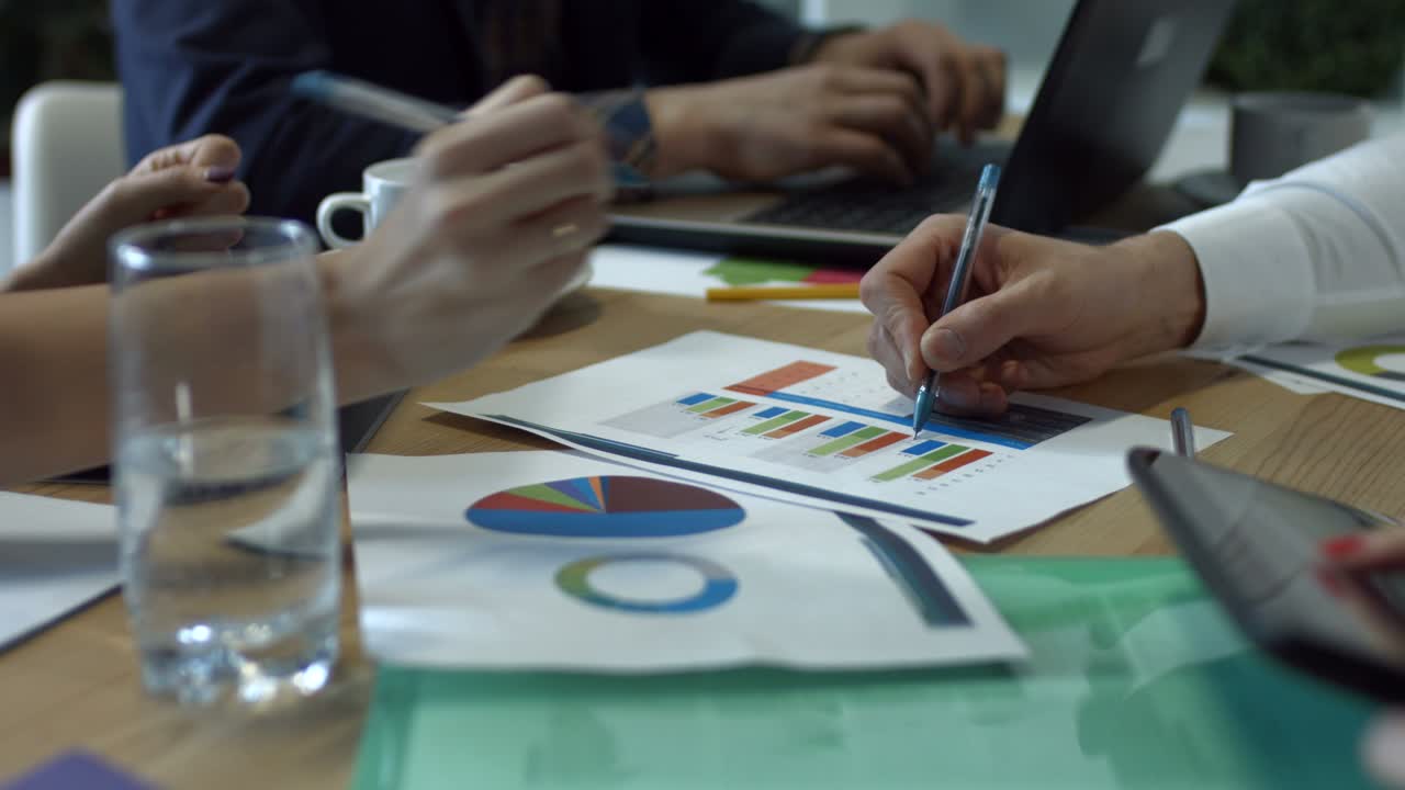 manos escribiendo en varios gráficos financieros en la mesa