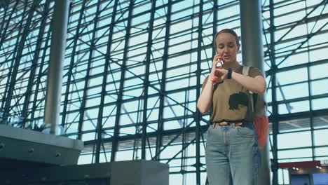 Young-beautiful-woman-standing-at-the-airport-calls-on-the-phone-on-the-background-of-the-scoreboard-with-information-about-the-departures.