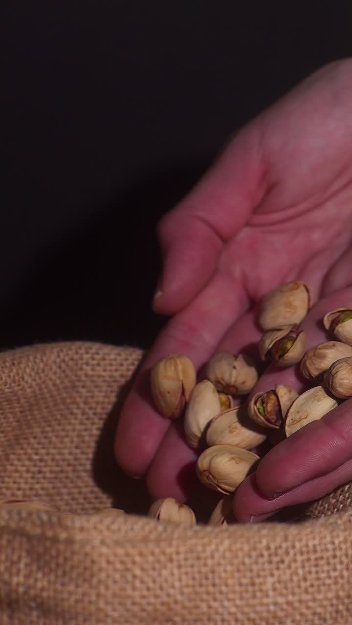 Slow-motion close-up of pistachios pouring gracefully from cupped hands onto burlap, ideal for healthy snack or natural product advertising. Warm tones and rich textures evoke freshness, authenticity
