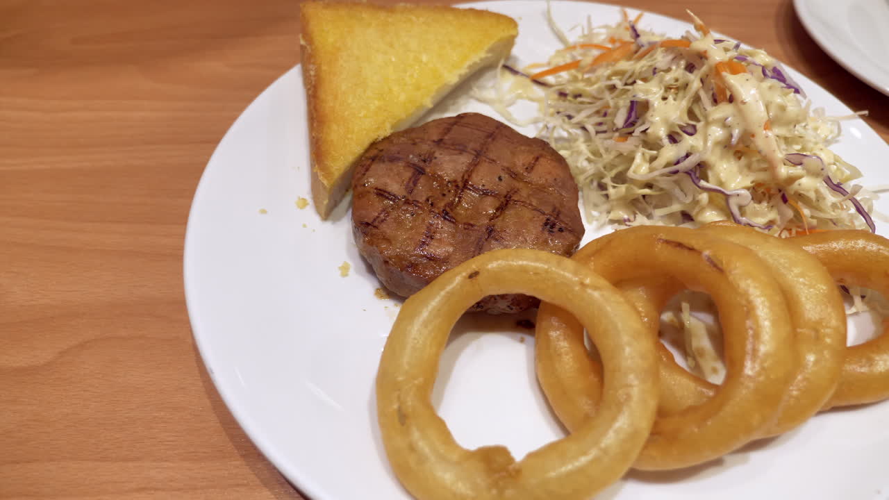 cerca de un plato lleno de anillos de cebolla, pan tostado, ensalada de coles y un corte de bistec de hamburguesa medio raro, servido en un restaurante en bangkok, tailandia