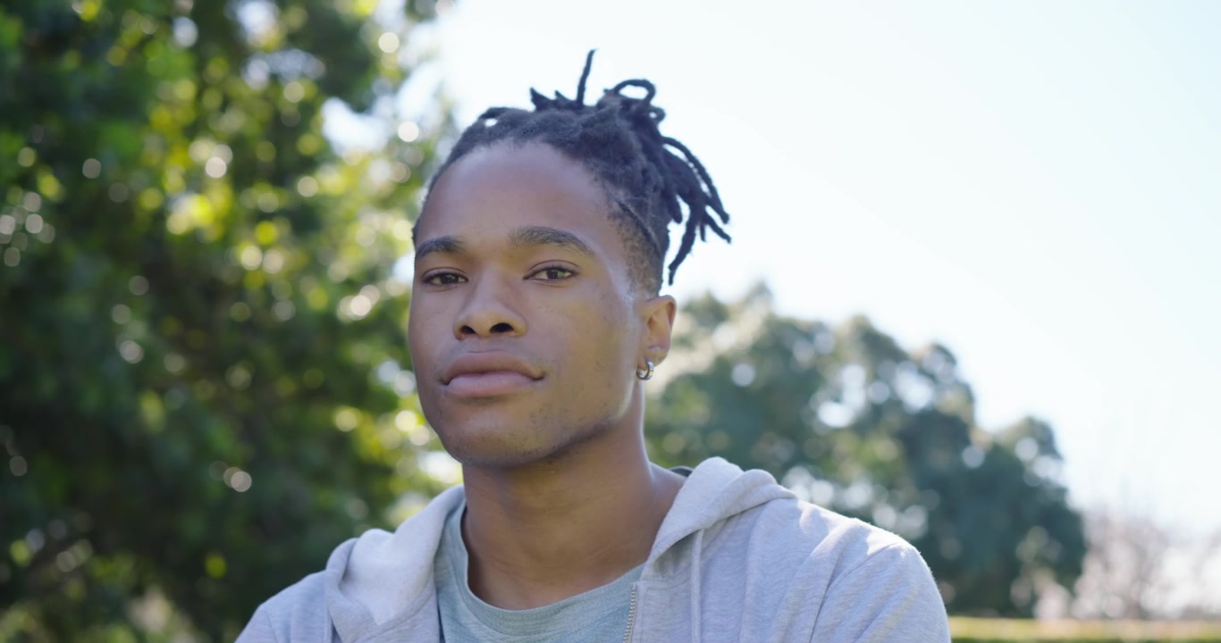 Sollys faller på en afrikansk mann som snur hodet, lukker øynene, tar en pause og tenker i hagen med hettegenser.