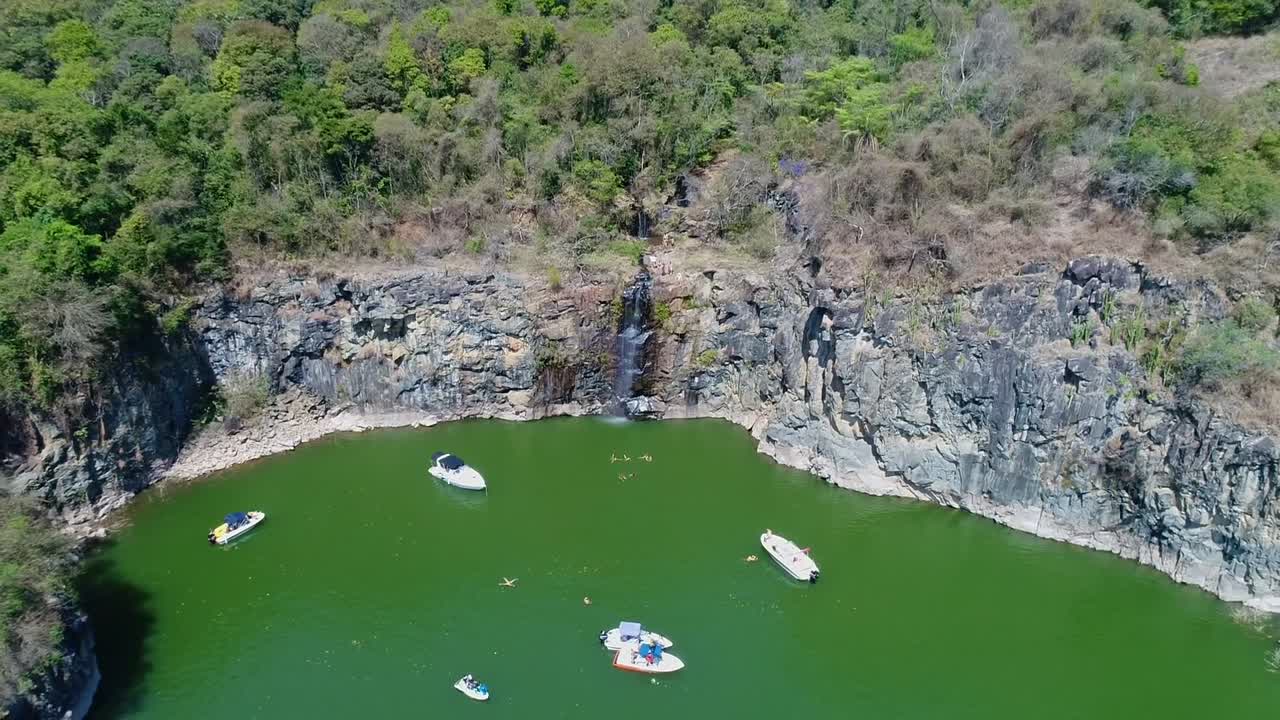 Cliff with waterfall and boats on shore on sunny day. Aerial