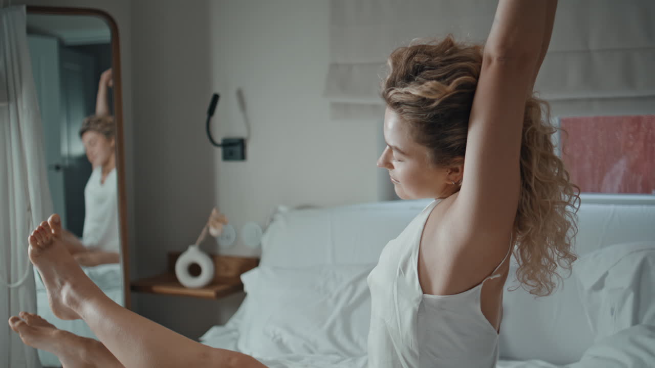 Serene woman stretching in bed welcoming calm day in bright bedroom closeup
