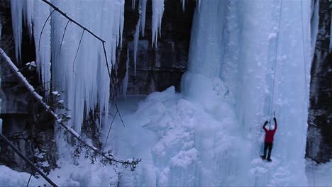 a man ice climbs a frozen waterfall