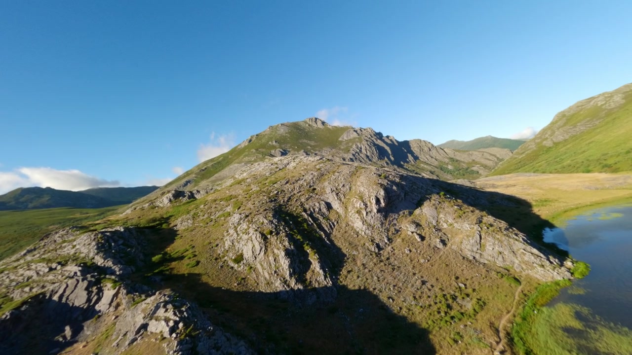 Dynaaminen FPV-dronekuvaa, joka liitää karun vuoristomaiseman ja kirkkaan sinisen järven yllä auringonlaskun aikaan. Tallentaa luonnon aidon kauneuden matkailu- ja kestävän kehityksen projekteihin.