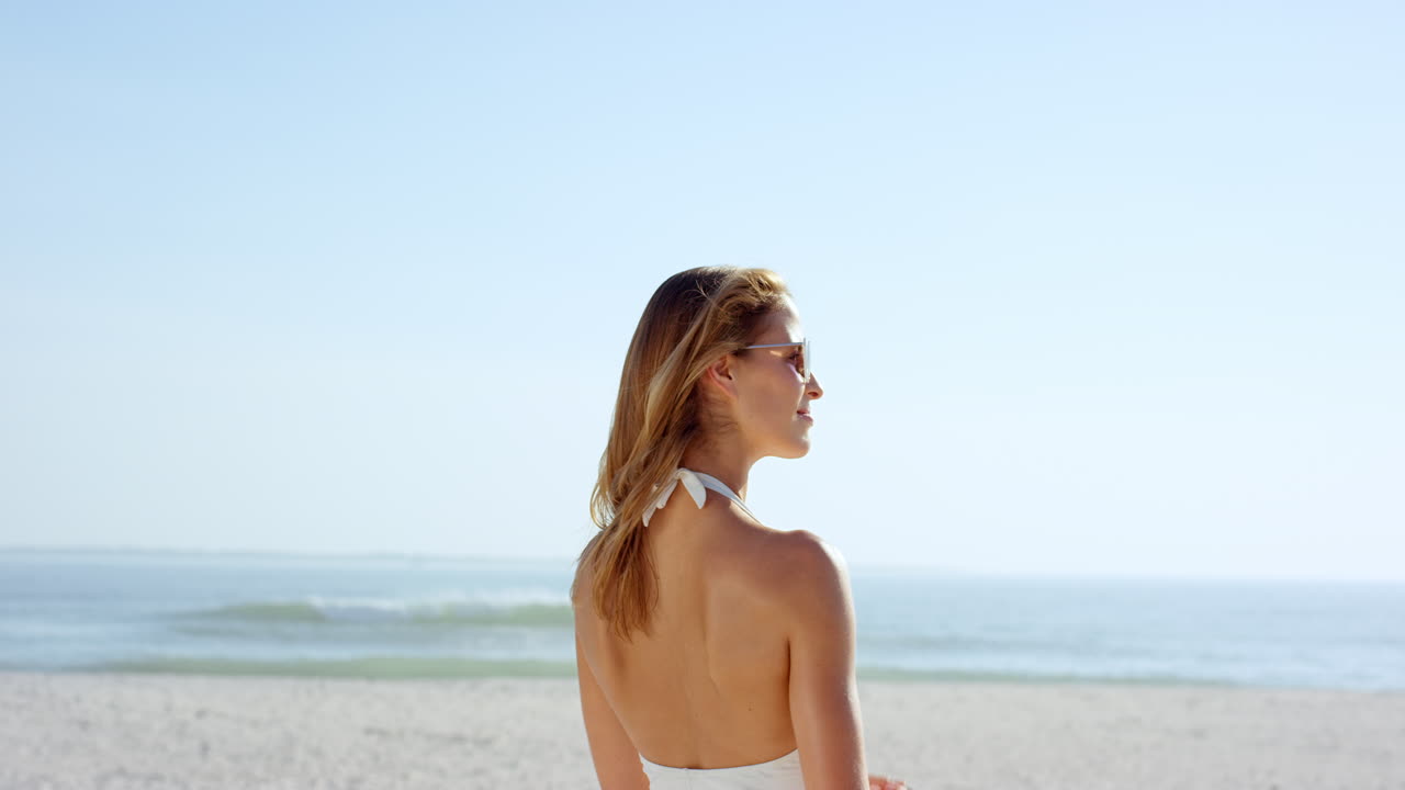 mujer hermosa atando el cabello en la playa vistiendo diseñador elegante traje de baño de una pieza tiene figura atlética delgada