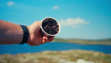 hand pours cup of compost with worms