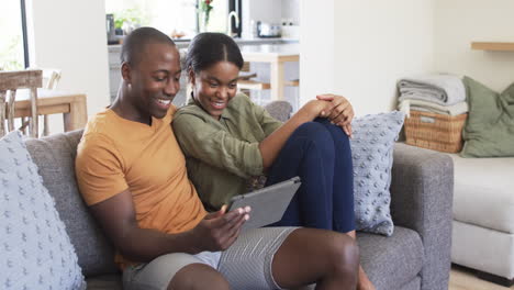 Una-Joven-Pareja-Afroamericana-Está-Ocupada-Con-Una-Tableta-En-El-Sofá-De-Casa