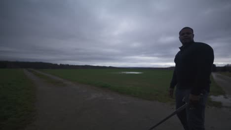 modern black swordsman warrior awaiting battle opponent in open field under grey sky, europe, 4k | muscular, intimidating, shadow, figure, blurry, dark clothes, powerful, adjusting stance, serious