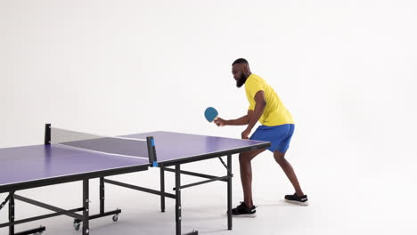 playing table tennis, african american man in yellow shirt hitting ball with paddle