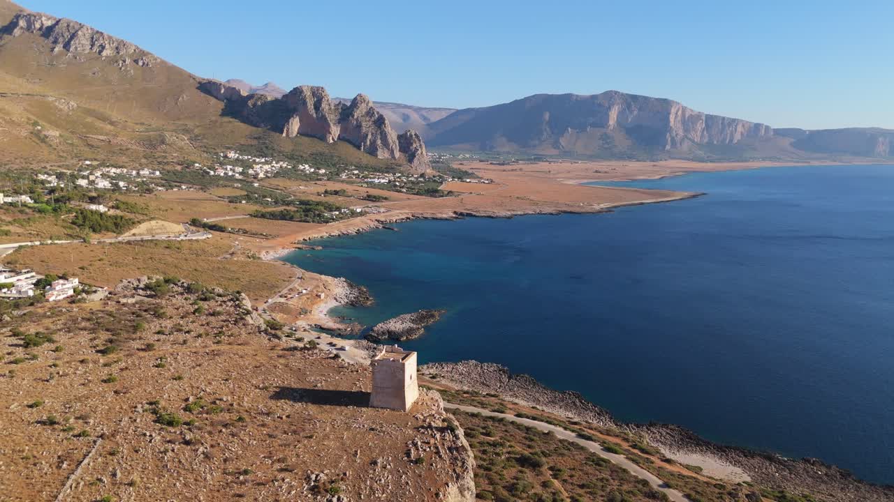 Drönarvy av Torre Isulidda på Sicilien som zoomar ut och visar kustklippor, öppet hav och bergslandskap under klar himmel