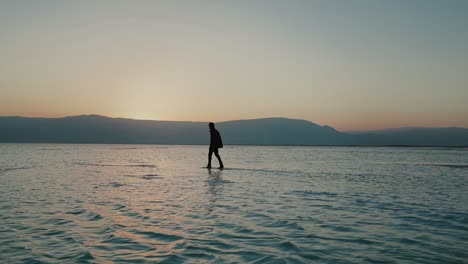 Silhouette-Eines-Mannes,-Der-Bei-Sonnenuntergang-In-Den-Untiefen-Des-Toten-Meeres-In-Israel-Spaziert