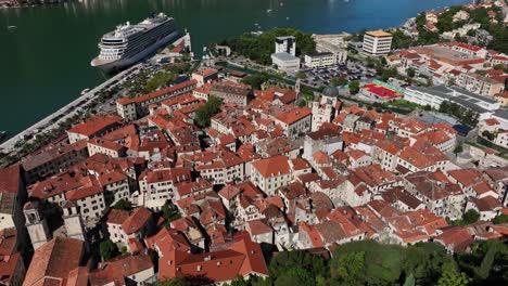 experience a smooth aerial left panning view across the rooftops of the old walled city of kotor in montenegro, revealing the intricate network of buildings and the surrounding landscape