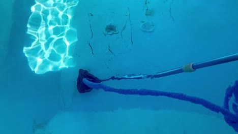 Top-transparent-view-of-vacuuming-dirty-swimming-pool-floor-with-aluminum-blue-telescopic-pole