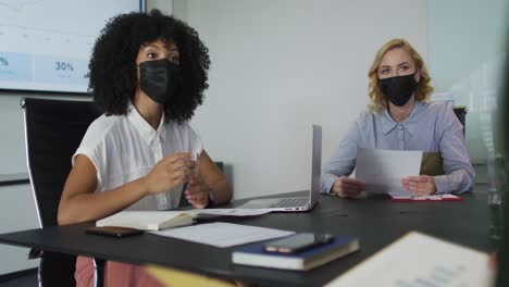 African-american-woman-wearing-mask-giving-presentation-in-meeting-room