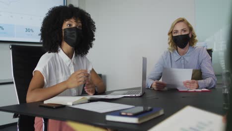 mujer afroamericana con máscara dando una presentación en la sala de reuniones