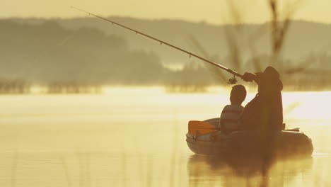 rear view of an old man with a hat and his grandson on a boat fishing with a rod on the lake on a cloudy morning