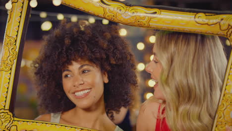 female friends having fun posing with photo booth photo frame at party in bar