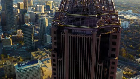 Aerial-drone-shot-slowly-descending-and-spiraling-around-the-top-of-the-Bank-of-America-skyscraper-during-sunset-in-downtown-Atlanta,-Georgia