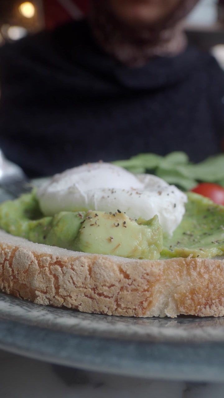Tagliare un uovo in camicia dal tuorlo morbido su un delizioso toast con avocado