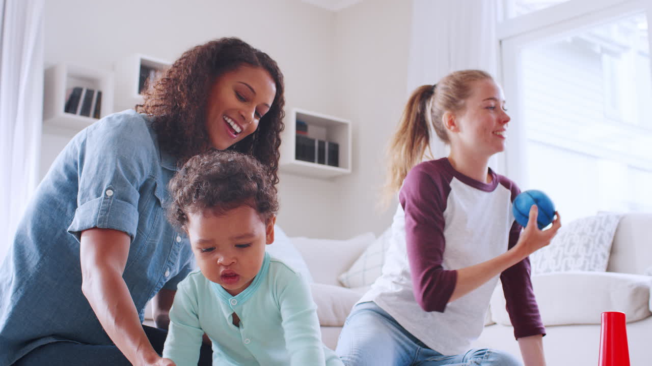 Donne bianche e nere che giocano con un bambino piccolo in salotto.