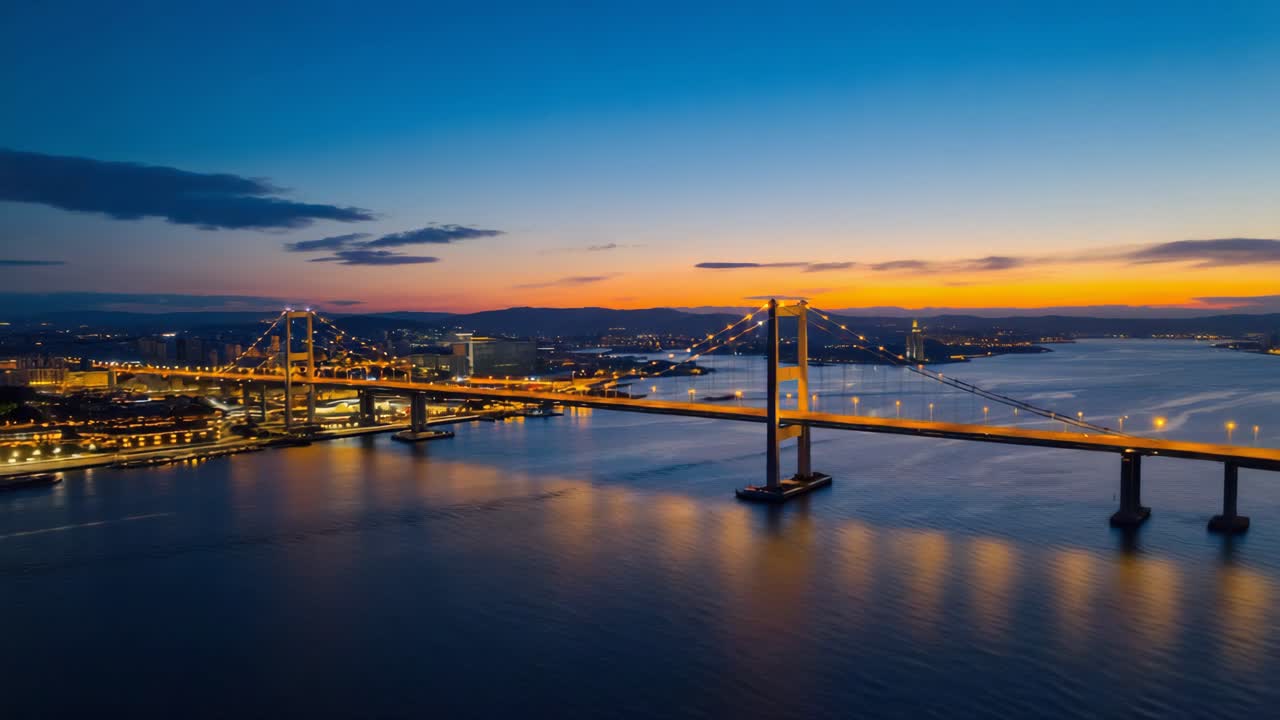 Illuminated Suspension Bridge at Dusk with Cityscape and Water Reflections
