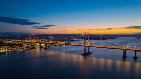 illuminated suspension bridge at dusk with cityscape and water reflections