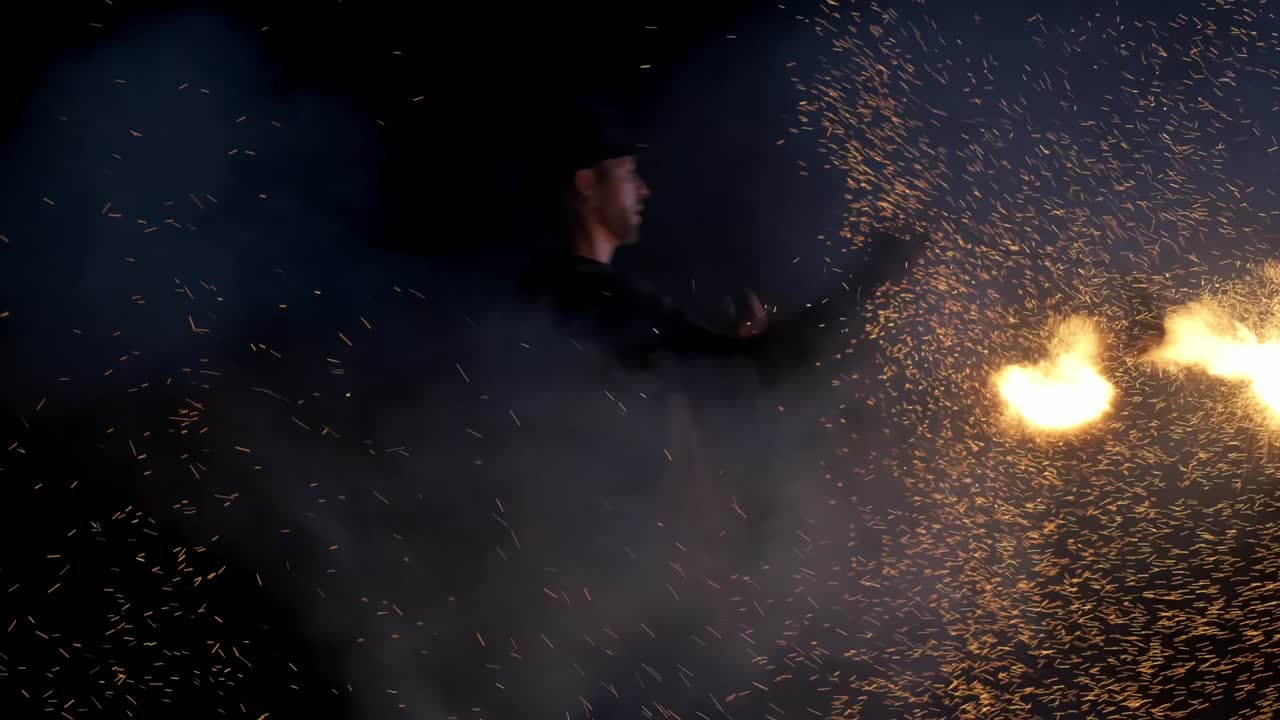 많은 불타는 불꽃이 다른 방향으로 날아갑니다. 남자는 거대한 불꽃을 숨쉬고 있습니다. 버려진 장소에서 불꽃 쇼 예술가들의 공연. 느린 모션.