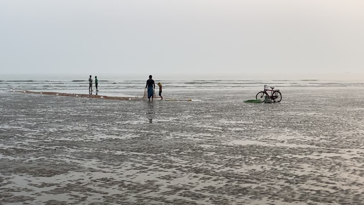силуэтный вид на пляж с волнами, люди с сетью для рыбалки перед велосипедом и несколько разговаривающих людей на пустом пляже в индии