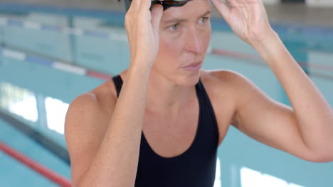 caucasian female swimmer athlete adjusts her swimming goggles at the pool