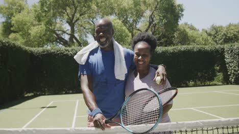 Porträt-Eines-Glücklichen-älteren-Afroamerikanischen-Paares-Mit-Tennisschlägern-Und-Ball-Auf-Dem-Tennisplatz