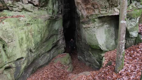 man coming through huge rock formations in mullerthal hiking trail in luxembourg - camera on front