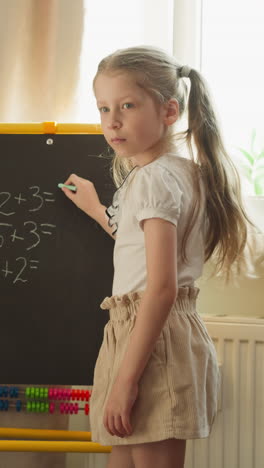 little schoolgirl stands at blackboard in room teaching toddler brother to solve math problems slow motion. boy thinks and raises hand telling answer