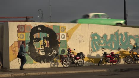 a car drives down a road near a building decorated with che revolutionary painting in communist cuba