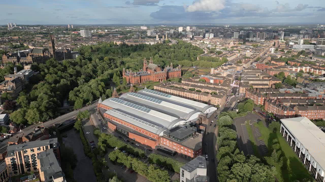 Aerial fly towards Kelvin Hall museum in natural parkland with Kelvingrove Art Gallery and Museum in background, Glasgow, Scotland, UK