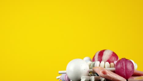 Isolated-in-front-of-a-bright-yellow-studio-background,-a-portion-of-colorful-kids-candy-rotates-slowly