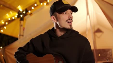 man plays the guitar and sings songs in a tent with light bulbs