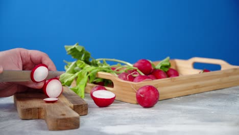 men's hands cut radish with a knife on a cutting board.