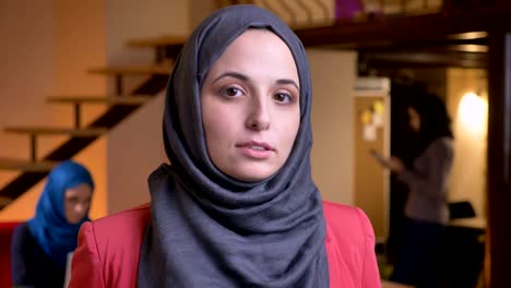 retrato en primer plano de una joven y hermosa mujer musulmana con hijab gris mirando pensativa en la contemplación de la cámara estando en el lugar de trabajo en el interior