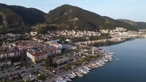 Impresionante-Vista-Aérea-De-La-Ciudad-De-Fethiye-Con-Barcos-Estacionados-En-La-Costa-Mediterránea-Y-Montañas-Al-Fondo,-Turquía