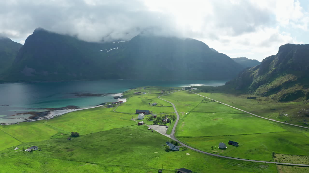 Aerial drone shot over the scenic Nordic Landscape of the Lofoten Islands in Norway. High view of green fields and the long stretching white sanded beach and the turquoise sea.