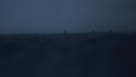 surfers sit in distance as water droplets bounce across ocean