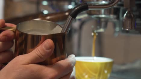 professional barista steaming milk with coffee dripping into cup in background