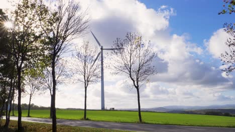 wind turbine standing still on hill blue sky with white clouds, sun breaks through trees