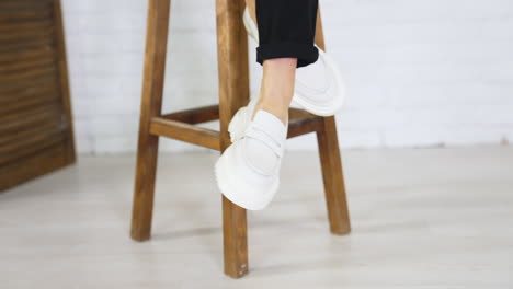 presentation of white shoes with plain massive soles. lady in modern footwear sits on the tabouret waving her feet. close up.