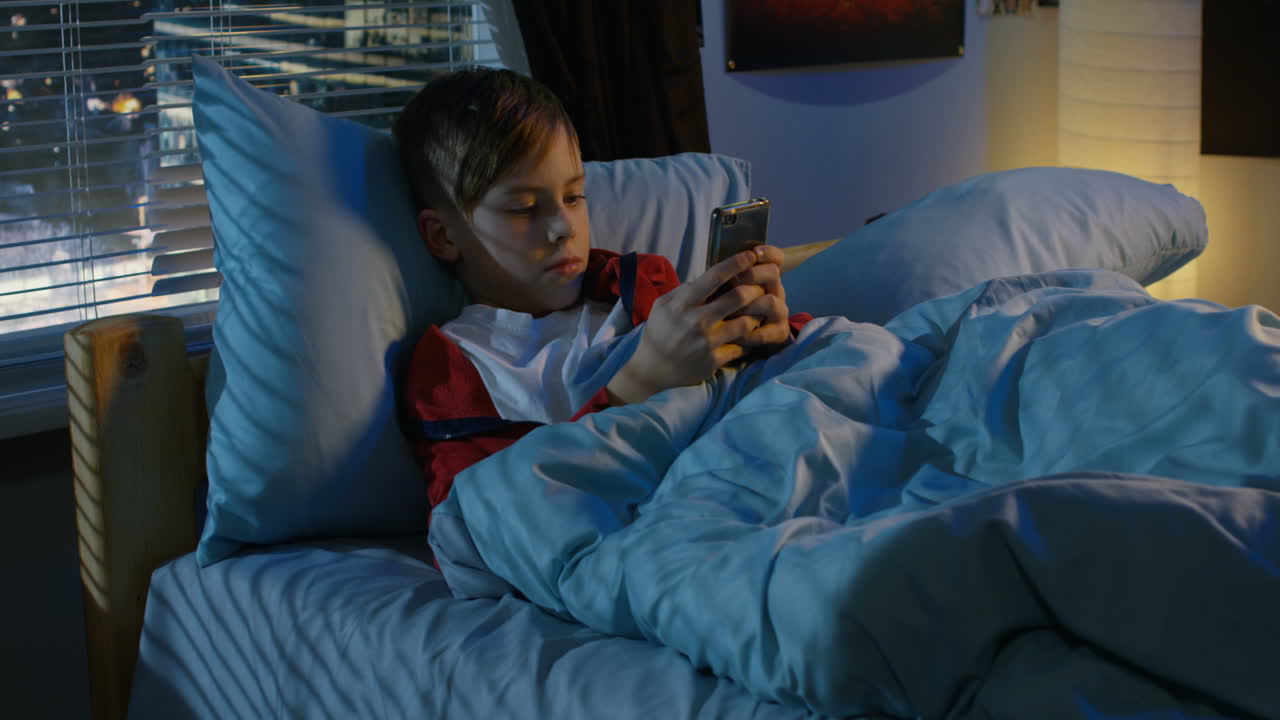 Young boy using smartphone in bed at night