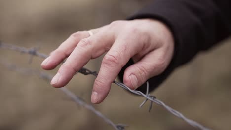 la mano del hombre se mueve lentamente sobre el alambre de púas