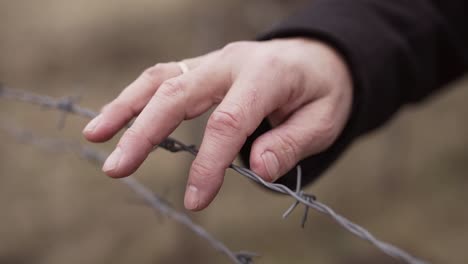 la main de l'homme se déplace lentement sur le fil de fer barbelé