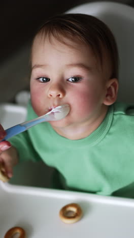 portrait of cute baby eating. small kid sitting on table and having breakfast. vertical video