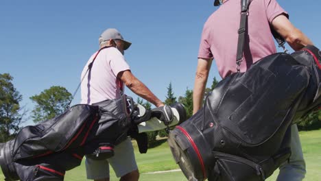 Two-caucasian-senior-man-wearing-face-masks-walking-with-their-golf-bags-at-golf-course